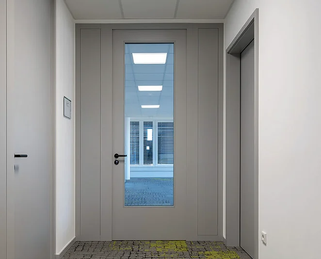 Graue Herholz-Tür mit Glasausschnitt in einem Büroflur, Ausführung für Rauch-, Brand- und Schallschutz-Anforderungen